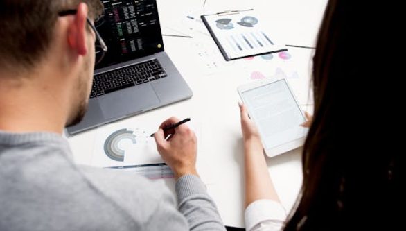 pexels-photo-5716000-5716000 Two business professionals analyzing financial reports using a laptop and tablet in a modern office setting.
