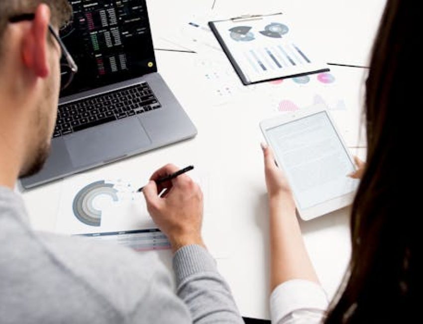 pexels-photo-5716000-5716000 Two business professionals analyzing financial reports using a laptop and tablet in a modern office setting.
